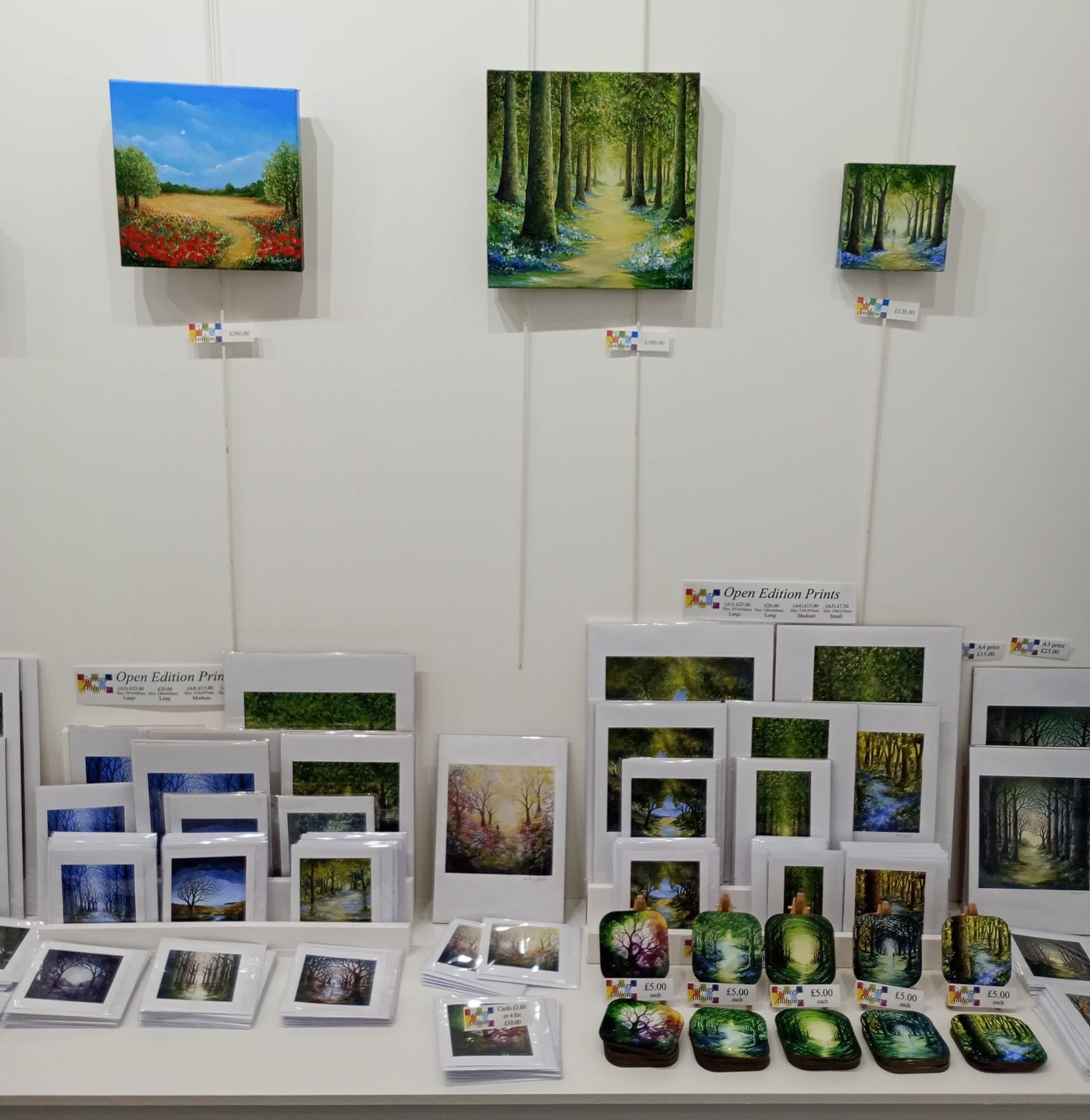 Display of various artworks including paintings and prints on a white wall.